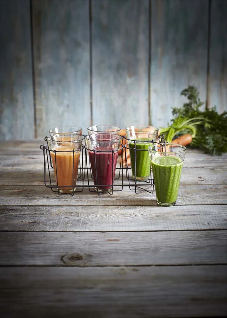Assorted array of smoothies in glasses on a rustic wood table with carrots in the background